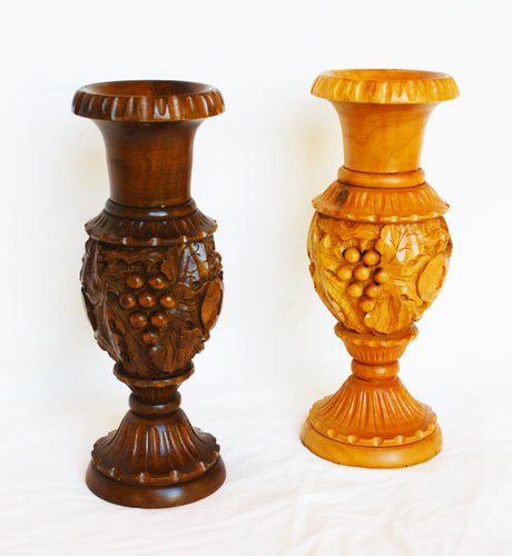 These vases are hand-carved by local artisans from indigenous woods, and come in mahogany and apricot colors. They are decorative with grapes and leaf carvings.  Suitable for displaying dried flowers. Dimensions are 11” tall and 4” deep.